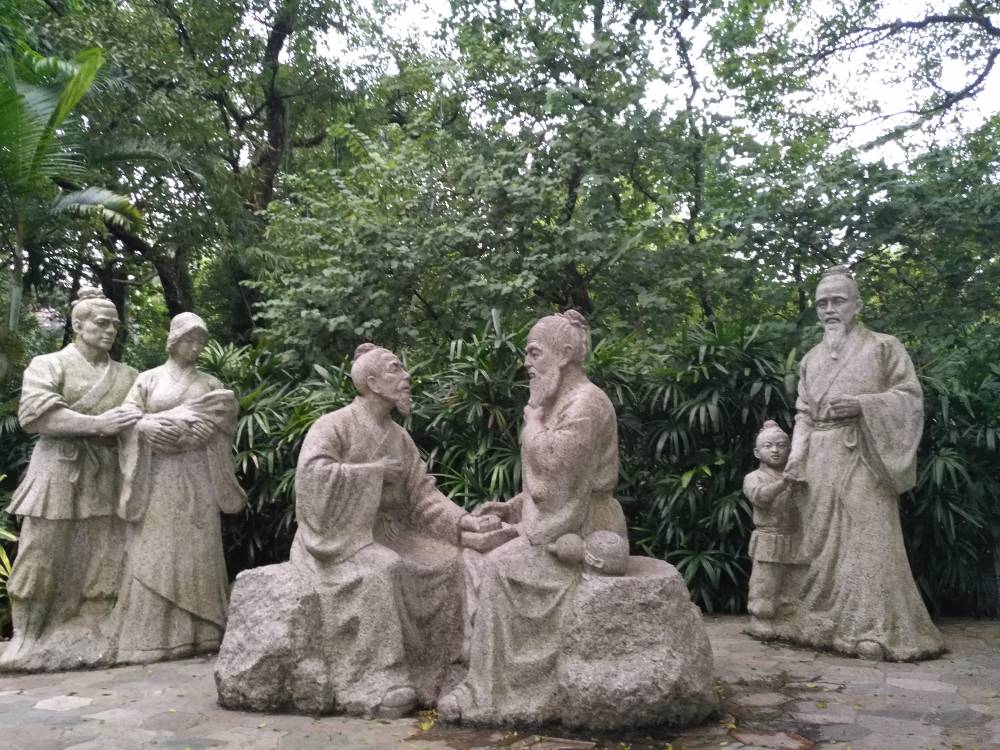 董奉悬壶济世坐石头上为病人诊脉造型黄锈石雕塑像杏林圣手抱孩子夫妇